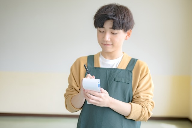 エプロンを着てメモを取る男性